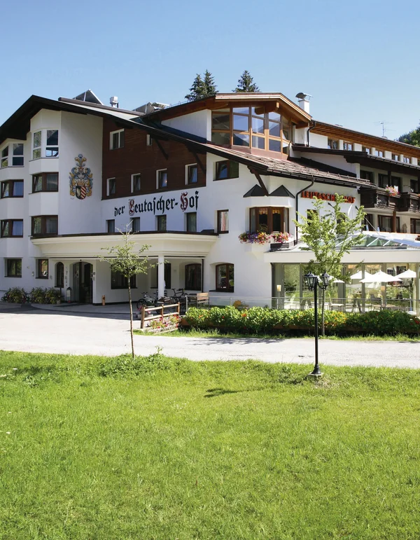 Unterkunft in Leutasch Großes Hotelgebäude mit Terrasse und grüner Wiese im Vordergrund