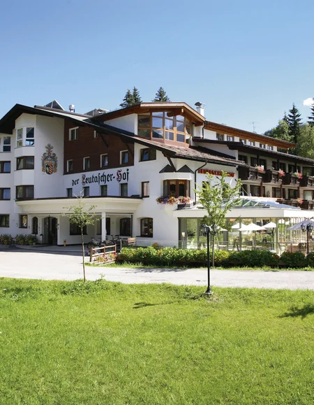 Von Herzen Gastgeber Großes Hotelgebäude mit Terrasse und grüner Wiese im Vordergrund