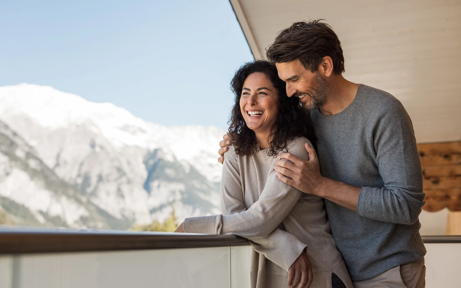Werfen Sie einen Blick in die Bildergalerie Glückliches Paar umarmt sich auf Balkon mit Bergblick im Hintergrund