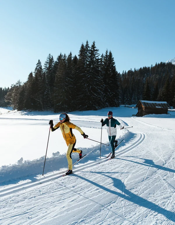 Urlaub auf Skiern: Ihr Langlaufhotel in Tirol Zwei Langläufer laufen auf einer sonnigen Schneepiste in den Bergen