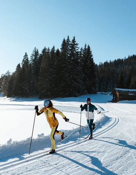 Urlaub in den Bergen: Ihr Naturhotel in Tirol Zwei Langläufer laufen auf einer sonnigen Schneepiste in den Bergen