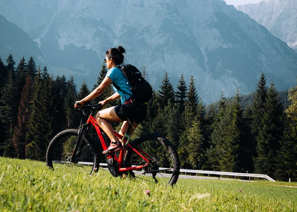 Wandertipps: Hier finden Sie die schönsten Touren! Frau fährt Mountainbike vor Berglandschaft und Wald