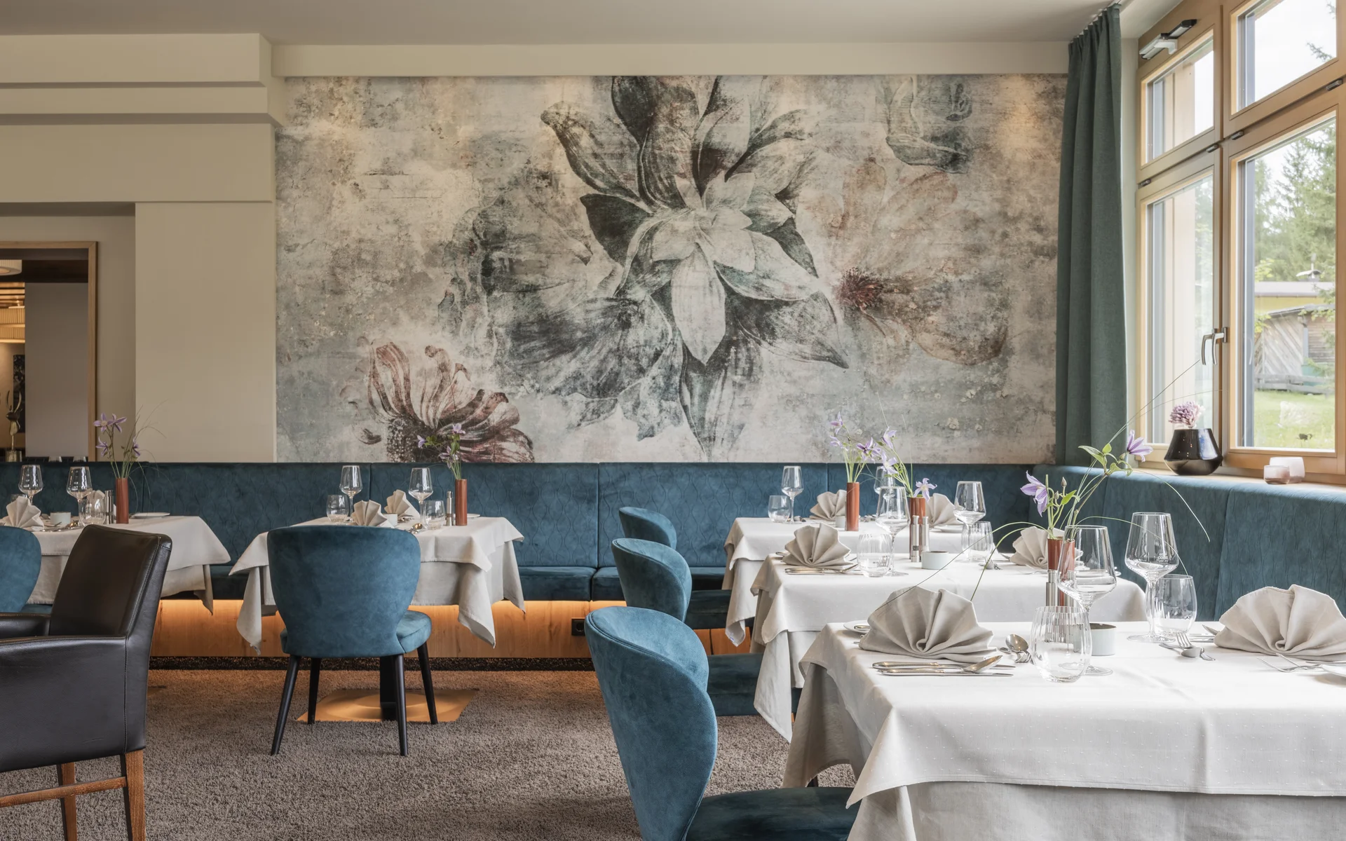 Werfen Sie einen Blick in die Bildergalerie Elegantes Restaurant mit gedeckten Tischen und floralem Wandbild