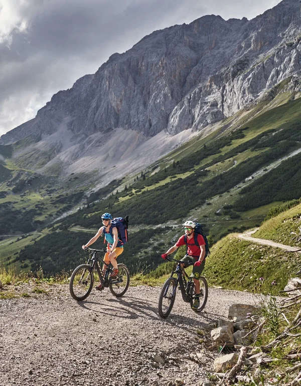 Urlaub auf zwei Rädern: Ihr Bikehotel in Tirol Zwei Radfahrer auf einem Bergweg mit Blick auf grüne Hügel und Felsen