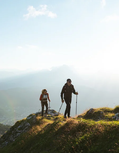 Urlaub in Bewegung: Ihr Aktivhotel in Tirol Zwei Wanderer auf einem grasbewachsenen Berg bei Sonnenlicht