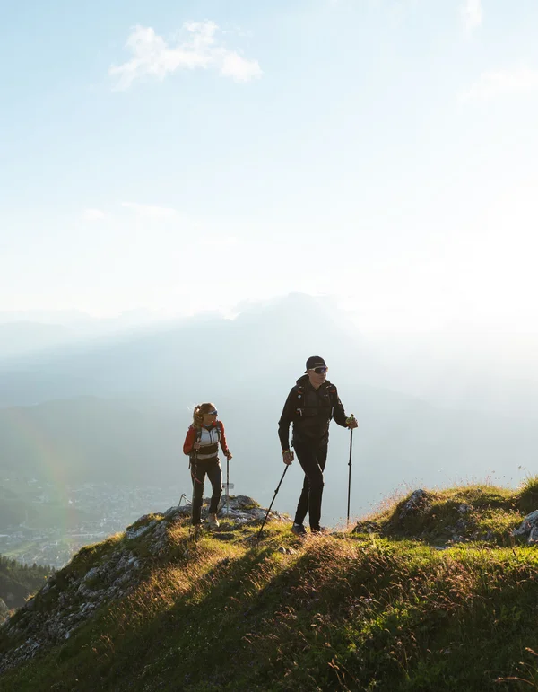 Urlaub auf zwei Rädern: Ihr Bikehotel in Tirol Zwei Wanderer auf einem grasbewachsenen Berg bei Sonnenlicht