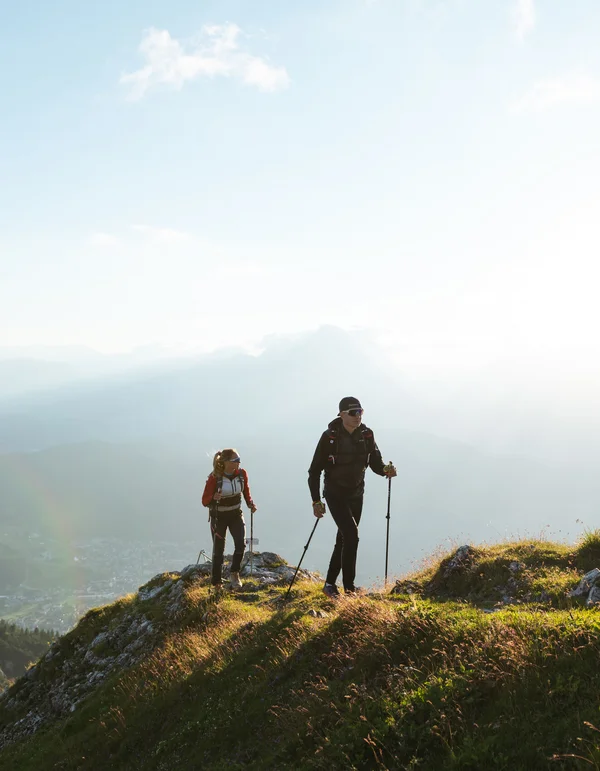 Ihr Wanderhotel in Tirol: Jetzt entdecken! Zwei Wanderer auf einem grasbewachsenen Berg bei Sonnenlicht