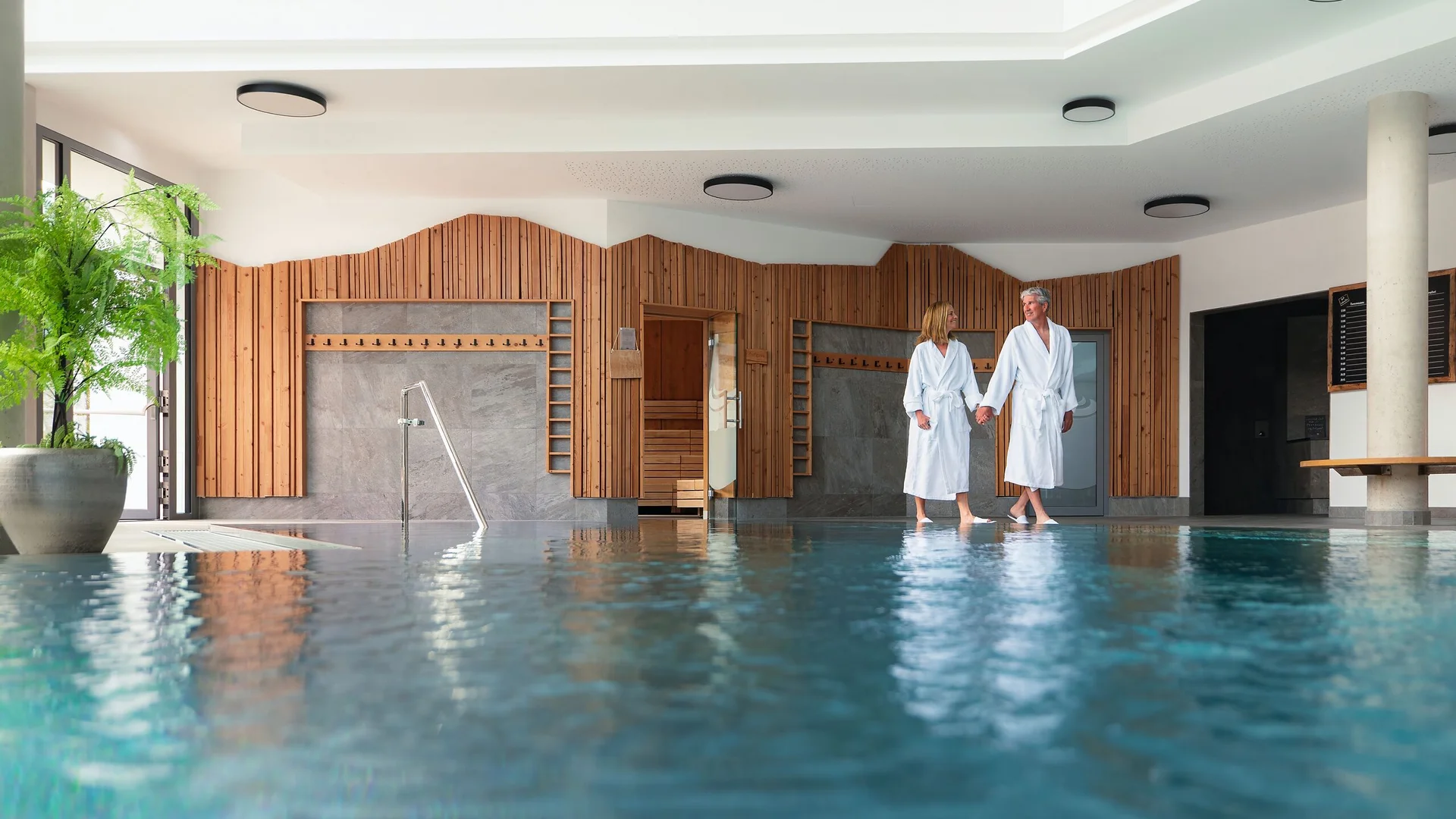 Erlebniswelt Alpenbad Leutasch Paar in Bademänteln am Innenpool im Wellnessbereich