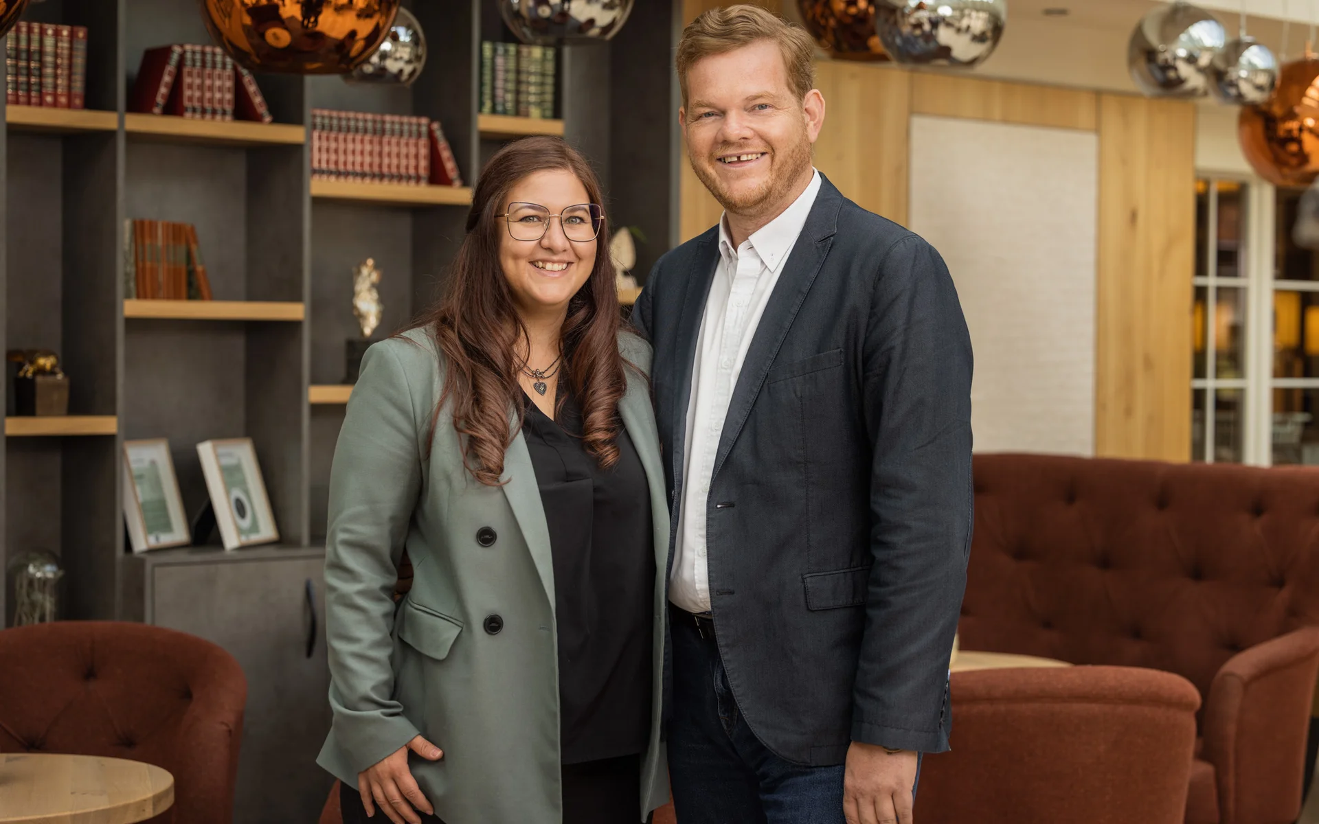 Werfen Sie einen Blick in die Bildergalerie Zwei lächelnde Personen in Business-Outfits in moderner Lounge