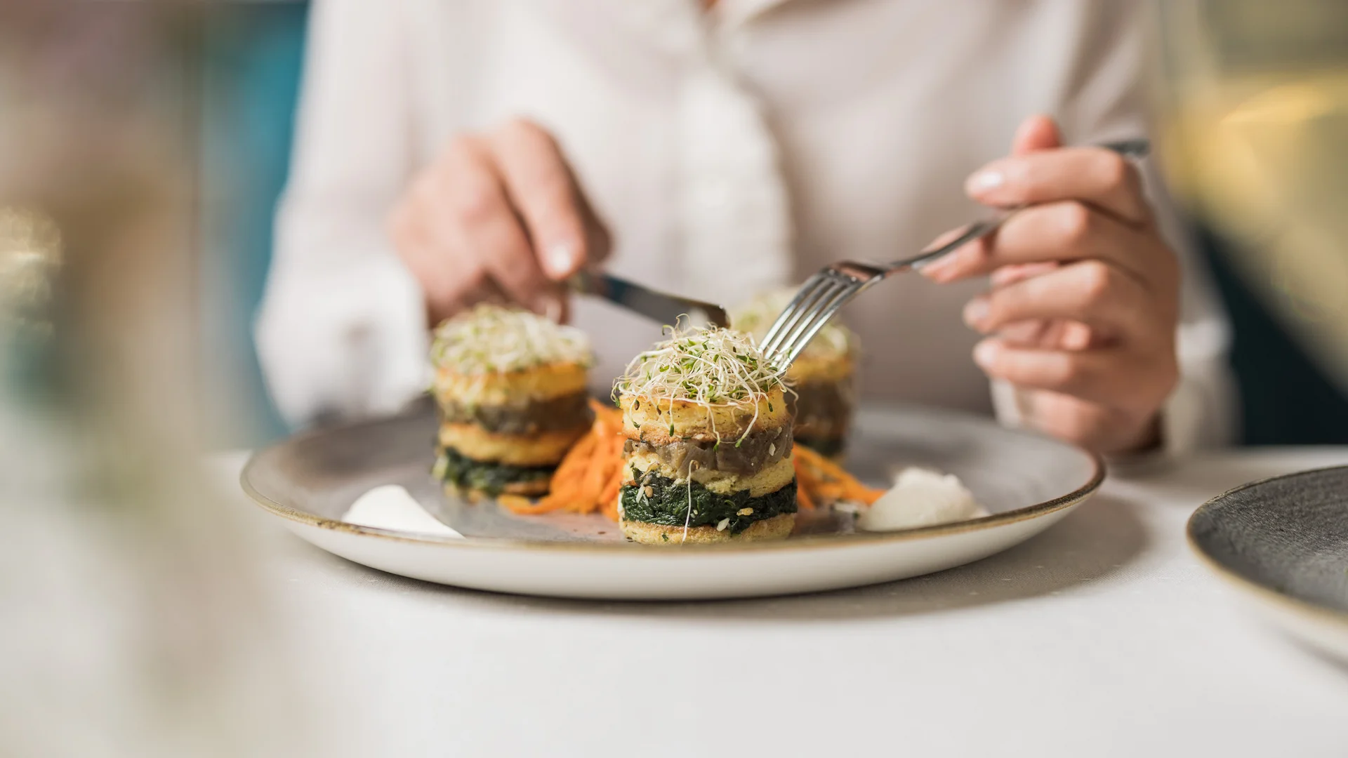 Das Hotel mit Bio-Küche in Tirol Person isst kunstvoll angerichtete vegane Speise mit Gabel und Messer