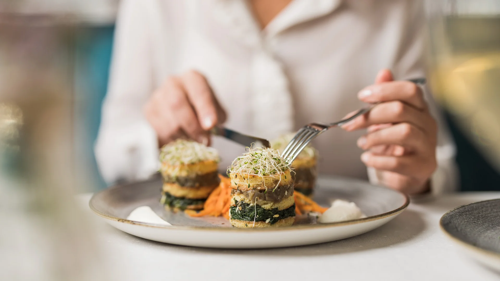 Das Hotel mit Bio-Küche in Tirol Person isst kunstvoll angerichtete vegane Speise mit Gabel und Messer