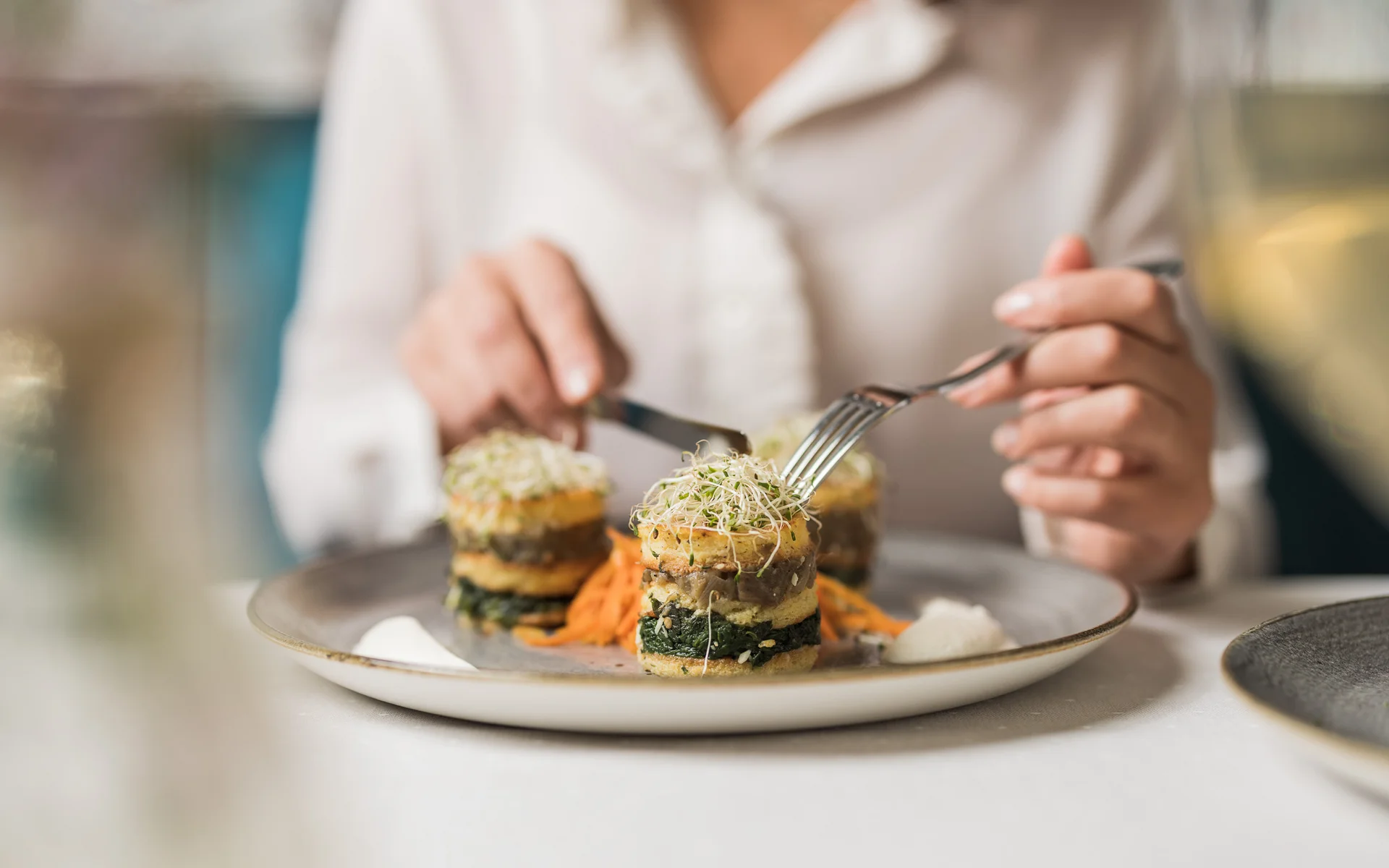Werfen Sie einen Blick in die Bildergalerie Person isst kunstvoll angerichtete vegane Speise mit Gabel und Messer