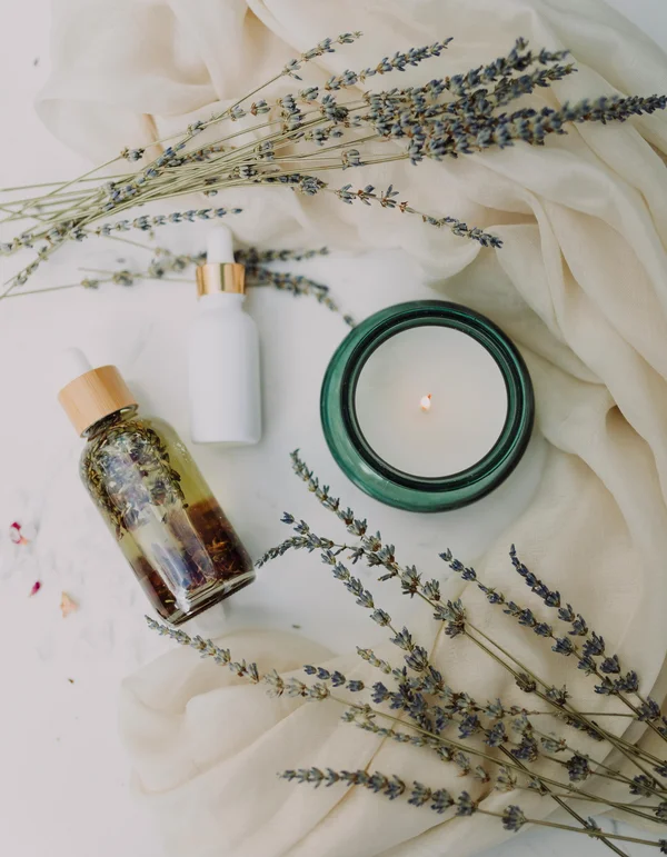 Wohlfühlprogramm oder Massage in Tirol? Lavendelzweige, Aromatherapieölflasche, Duftkerze und weißes Tuch auf Marmor