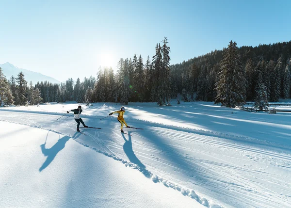 Urlaub auf Skiern: Ihr Langlaufhotel in Tirol Zwei Skifahrer fahren auf verschneiter Strecke im sonnigen Winterwald