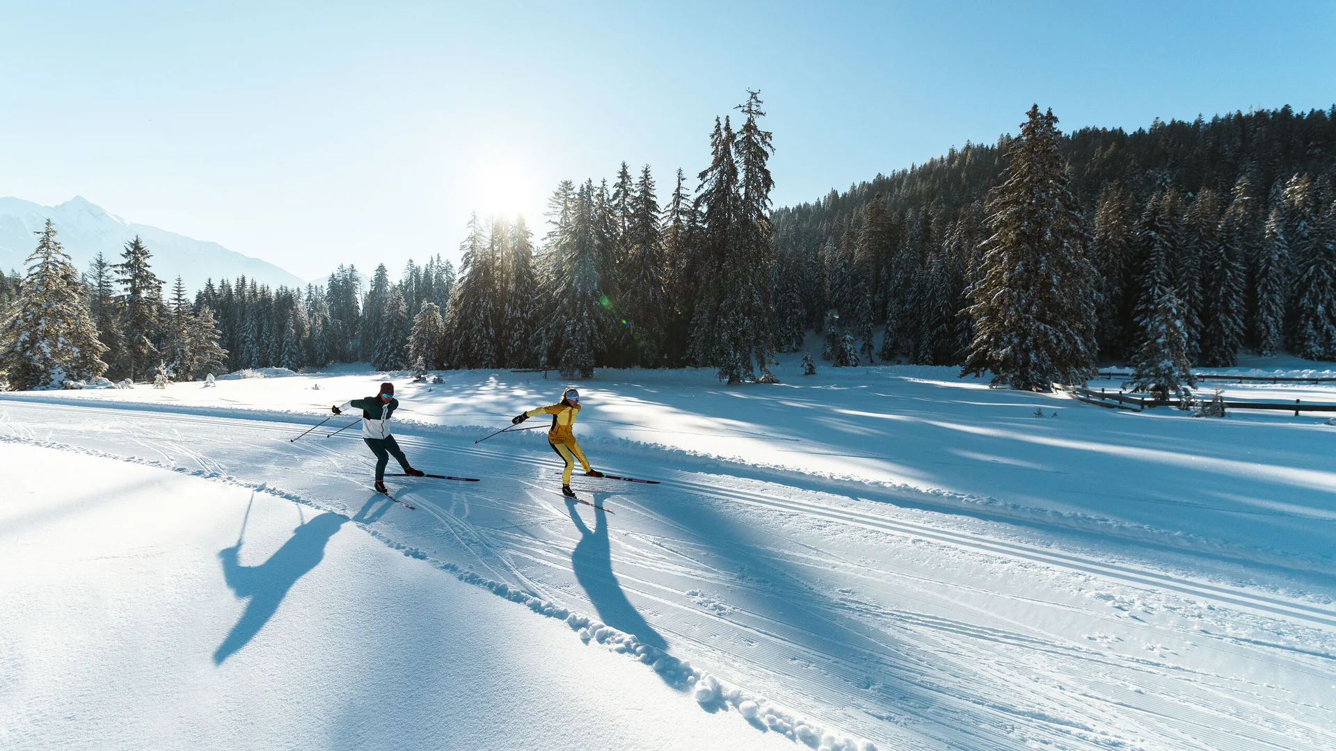 Urlaub in Bewegung: Ihr Aktivhotel in Tirol Zwei Skifahrer fahren auf verschneiter Strecke im sonnigen Winterwald