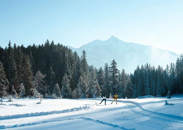 Urlaub auf Skiern: Ihr Langlaufhotel in Tirol Zwei Skifahrer auf verschneiter Loipe vor Tannenwald und Bergkulisse