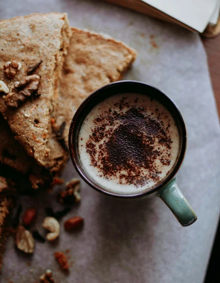 Ihre Almhütte in Tirol Tasse Kaffee mit Milchschaum und Nüssen neben Vollkornbrot