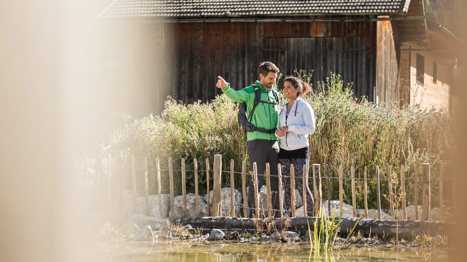 Urlaub in Bewegung: Ihr Aktivhotel in Tirol Paar genießt Aussicht nahe Holzzaun und Teich vor Hütte in Natur