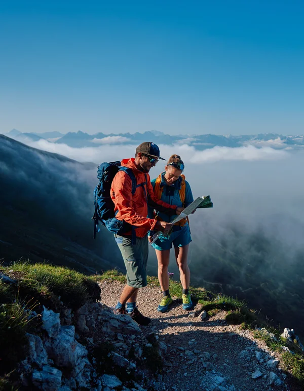 Alle Touren auf einen Blick Zwei Wanderer mit Karte auf einem Bergweg über den Wolken