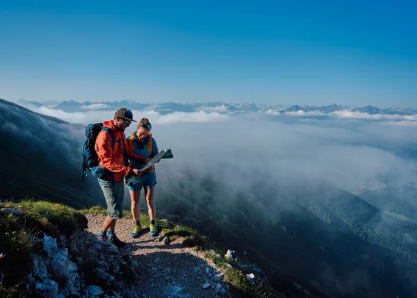 Wandertipps: Hier finden Sie die schönsten Touren! Zwei Wanderer mit Karte auf einem Bergweg über den Wolken