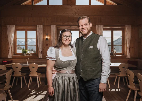 Ihre Almhütte in Tirol Paar in traditioneller Tracht in einem Holzhaus mit Bergblick