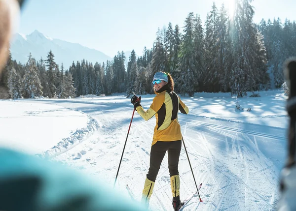 Urlaub auf Skiern: Ihr Langlaufhotel in Tirol Frau beim Langlaufen im verschneiten Wald mit Bergblick bei Sonnenschein