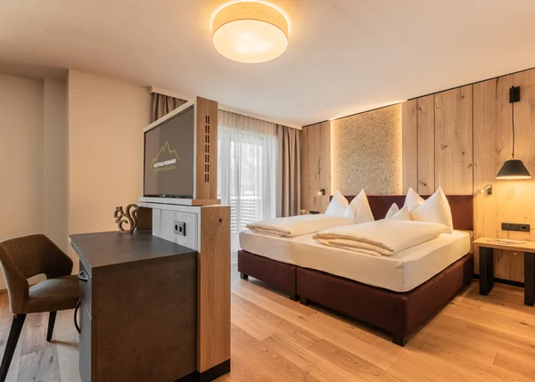 Vom Familienbetrieb zum echten Biohotel Modernes Hotelzimmer mit Doppelbett, Holzwänden und Schreibtisch mit TV