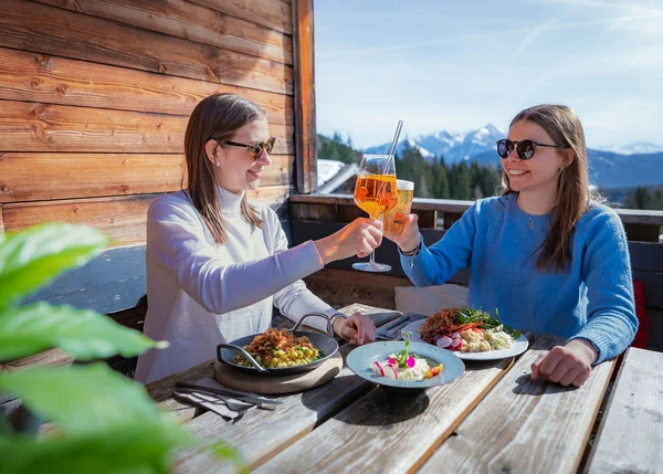 Ihre Almhütte in Tirol Zwei Frauen stoßen mit Getränken auf einer Terrasse mit Bergblick an