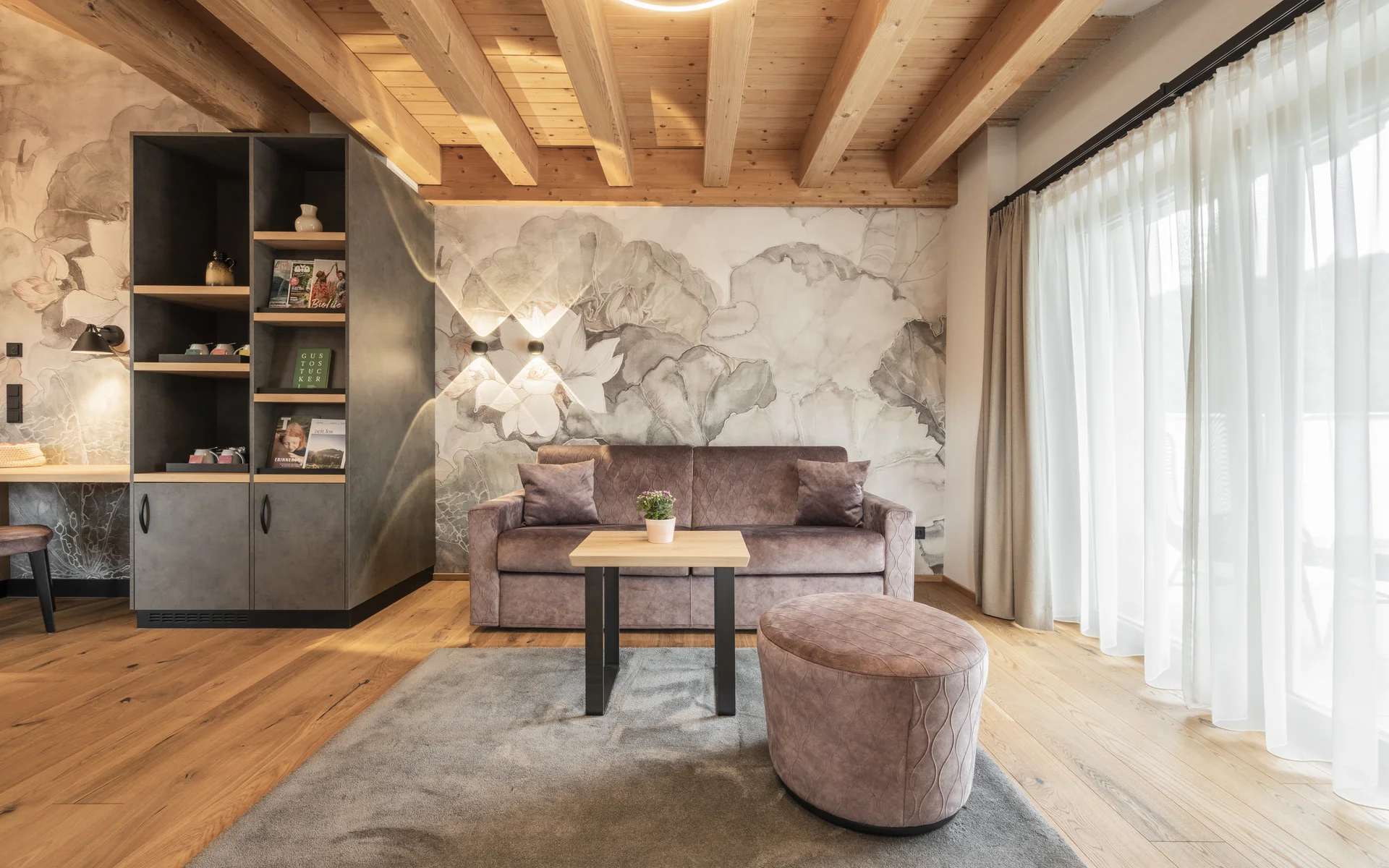 Werfen Sie einen Blick in die Bildergalerie Gemütliches Wohnzimmer mit Holzdecke, Sofa, Hocker und großem Fenster mit Vorhängen