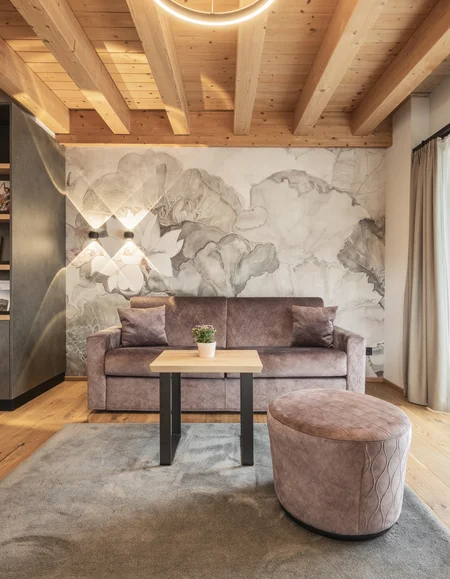 Entspannen im Hotel mit Sauna in Österreich Gemütliches Wohnzimmer mit Holzdecke, Sofa, Hocker und großem Fenster mit Vorhängen