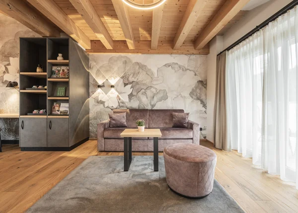 Vom Familienbetrieb zum echten Biohotel Gemütliches Wohnzimmer mit Holzdecke, Sofa, Hocker und großem Fenster mit Vorhängen