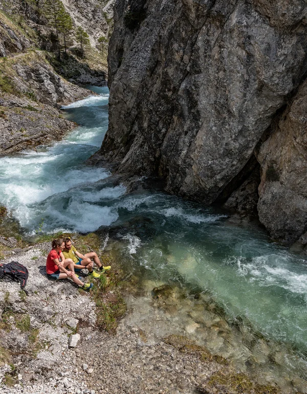 Erlebniswelt Alpenbad Leutasch Zwei Wanderer sitzen an einem Fluss in einer felsigen Schlucht