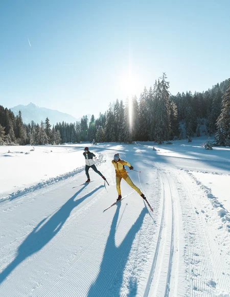Urlaub in Bewegung: Ihr Aktivhotel in Tirol Zwei Langläufer bei sonnigem Wintertag auf präparierter Spur im verschneiten Wald