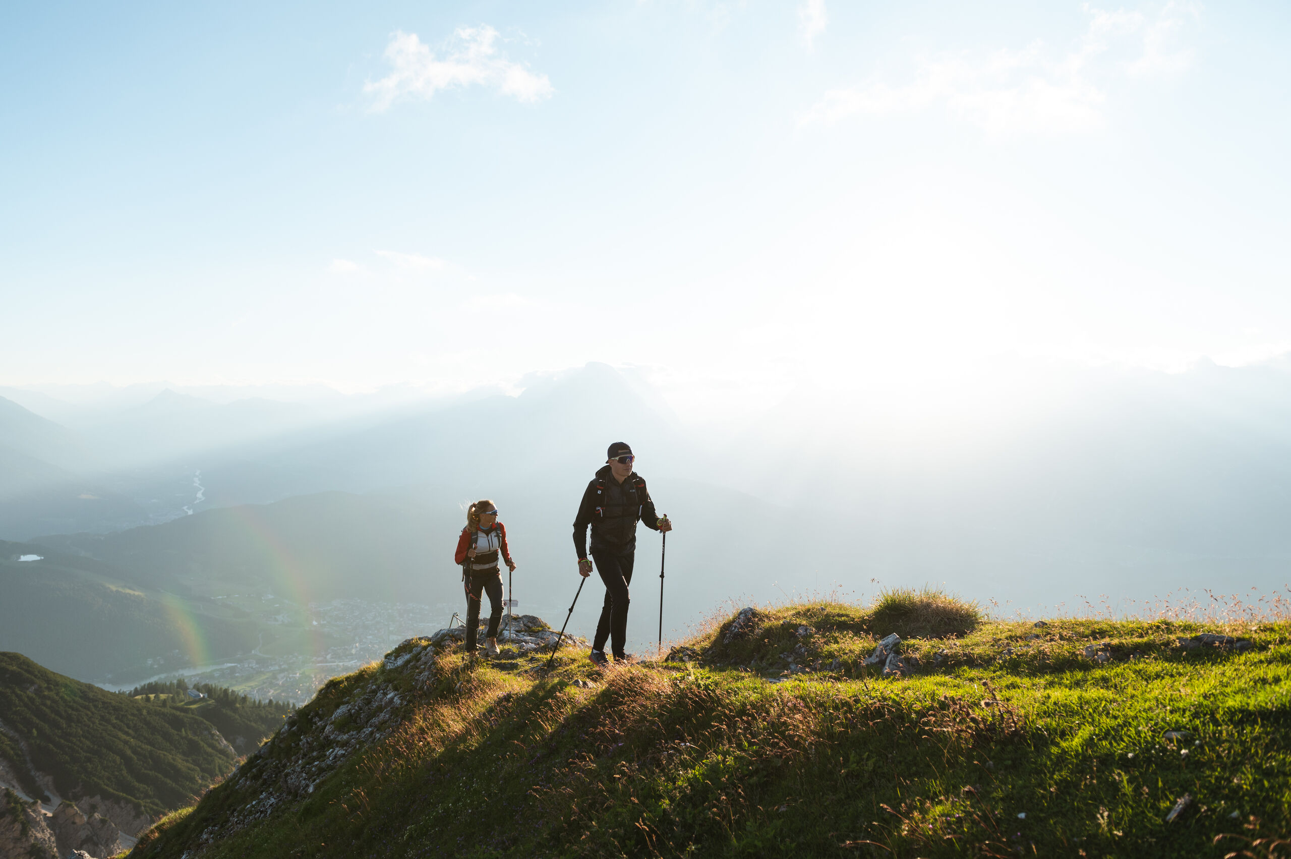 Werfen Sie einen Blick in die Bildergalerie Zwei Wanderer auf einem grasbewachsenen Berg bei Sonnenlicht