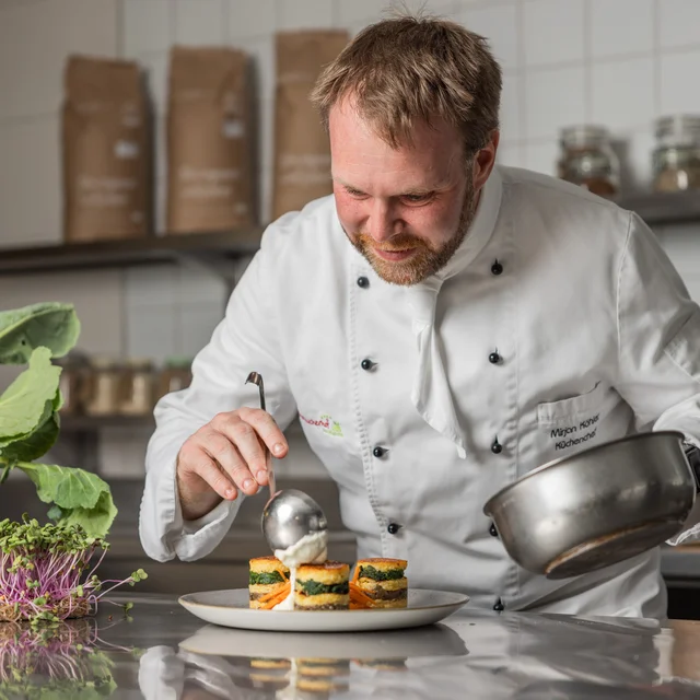 Biohotel Leutascherhof – Ihr Kraftort in den Tiroler Alpen Koch dekoriert Teller mit drei kleinen Schichtgerichten in professioneller Küche