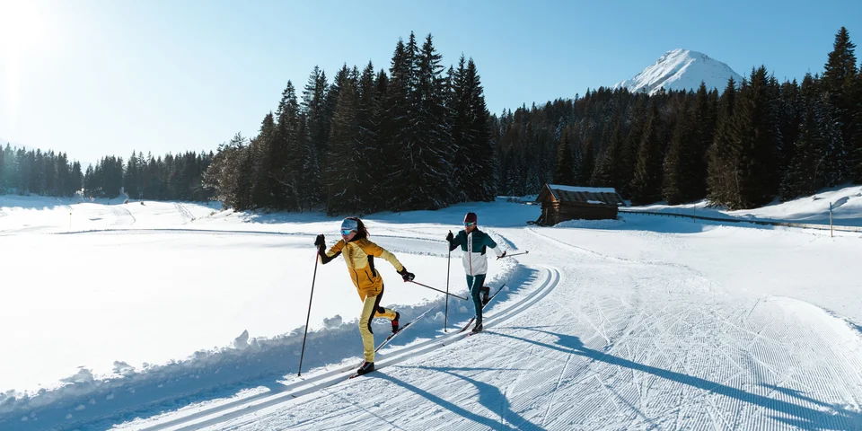Biohotel Leutascherhof – Ihr Kraftort in den Tiroler Alpen Zwei Langläufer laufen auf einer sonnigen Schneepiste in den Bergen