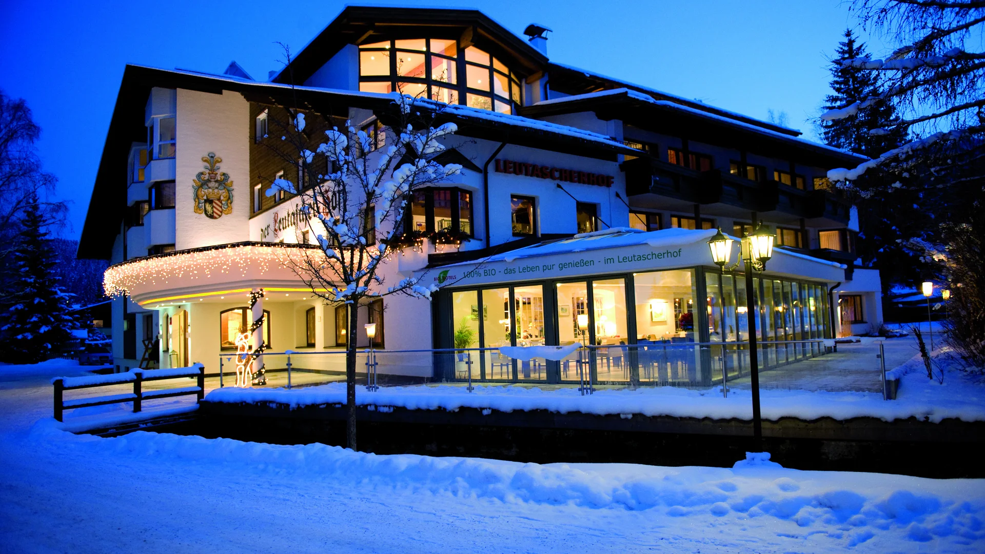 Biohotel Leutascherhof – Ihr Kraftort in den Tiroler Alpen Beleuchtetes Hotel im Schnee bei Abenddämmerung