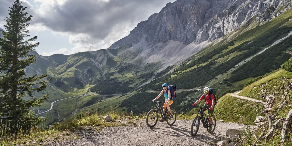 Biohotel Leutascherhof – Ihr Kraftort in den Tiroler Alpen Zwei Radfahrer auf einem Bergweg mit Blick auf grüne Hügel und Felsen