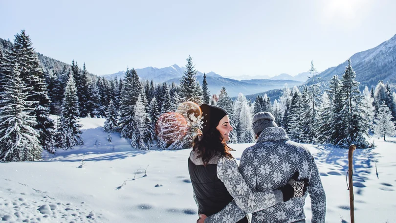 Biohotel Leutascherhof – Ihr Kraftort in den Tiroler Alpen Paar umarmt sich in verschneiter Winterlandschaft vor Bergen