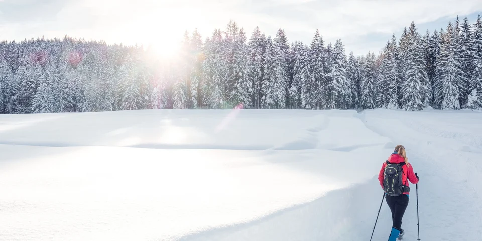 Biohotel Leutascherhof – Ihr Kraftort in den Tiroler Alpen Person wandert mit Stöcken auf verschneitem Weg im Winterwald bei Sonnenschein