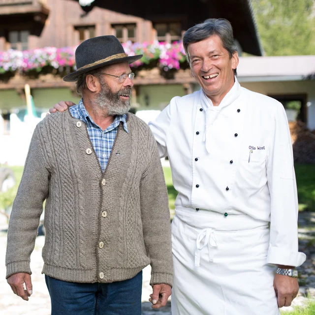 Biohotel Leutascherhof – Ihr Kraftort in den Tiroler Alpen Bauer und Koch lachen zusammen vor einem Bauernhof und Traktor