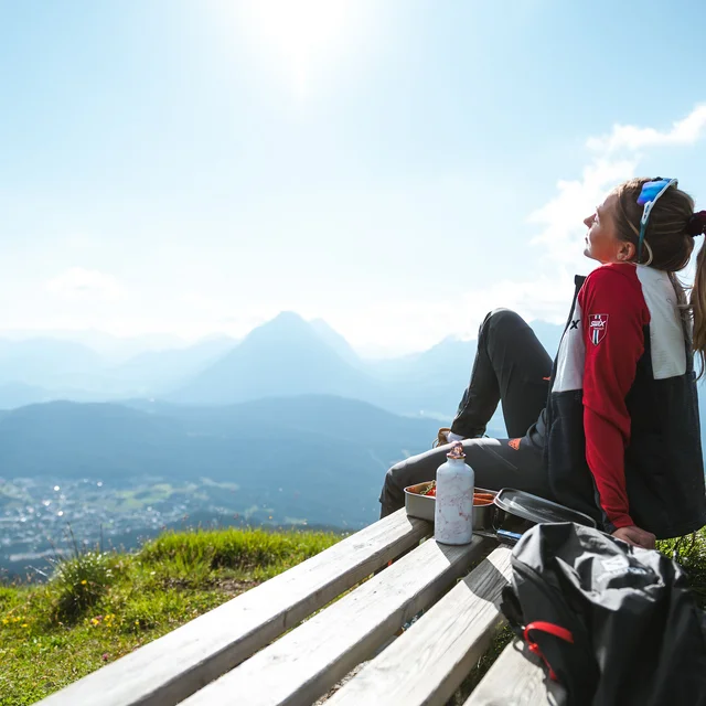 Biohotel Leutascherhof – Ihr Kraftort in den Tiroler Alpen Frau sitzt auf Bank mit Bergblick bei sonnigem Wetter