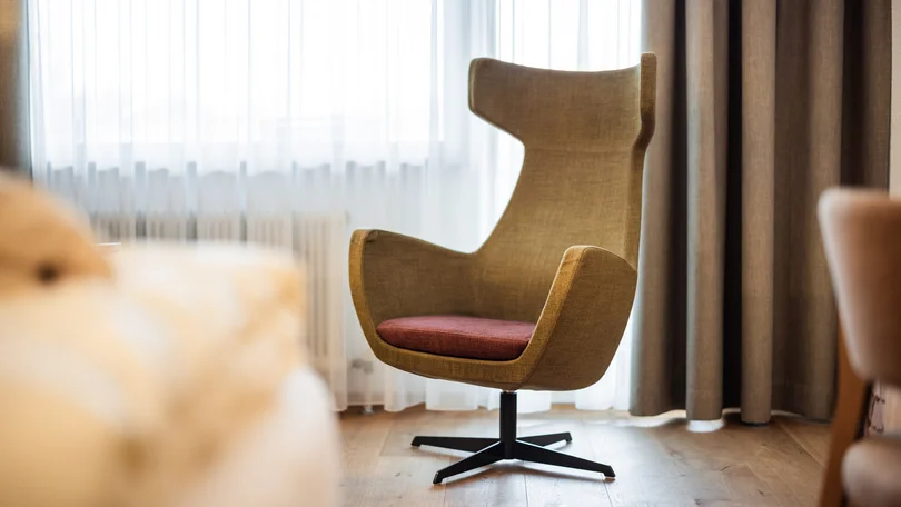 Biohotel Leutascherhof – Ihr Kraftort in den Tiroler Alpen Moderner brauner Sessel vor Fenster mit weißen Vorhängen